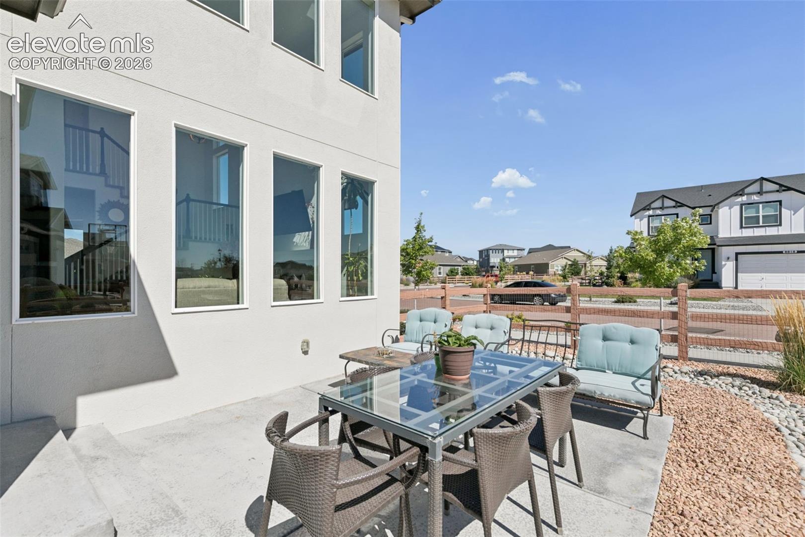 Exterior stucco finish, multiple large windows, concrete patio, gravel landscaping, and a wooden fence