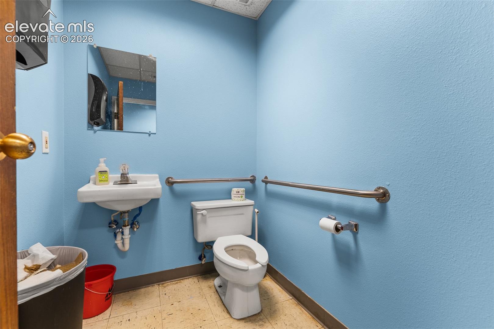 Restroom featuring a wall-mounted vitreous china sink, standard-height toilet, square wall-mounted mirror, and horizontal stainless steel grab bars