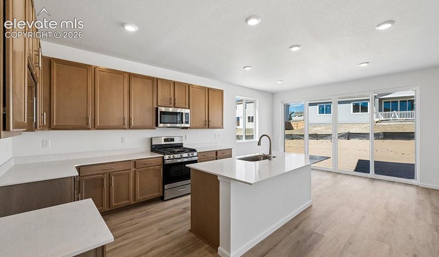 Kitchen featuring wood-finish cabinetry, quartz countertops, a center island with an integrated sink, stainless steel appliances, and large sliding glass doors