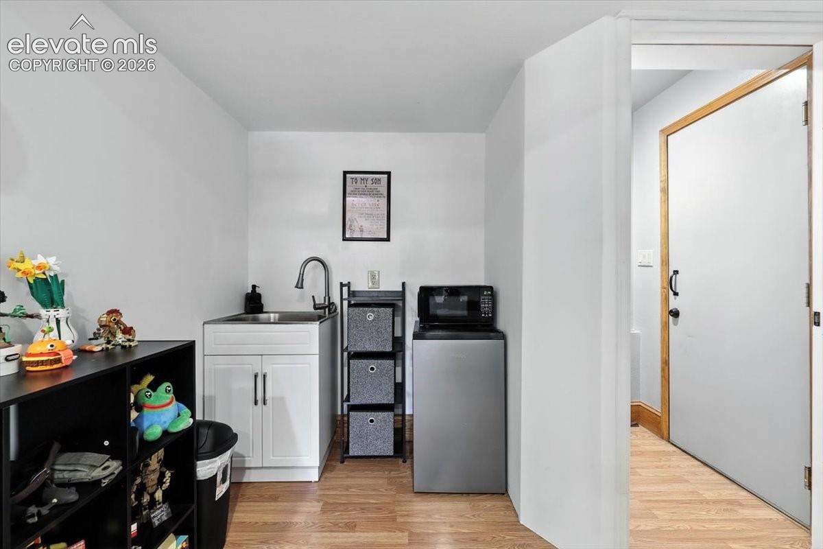 Wet bar featuring white cabinetry, a stainless steel sink with a high-arch gooseneck faucet, and wood-finish flooring