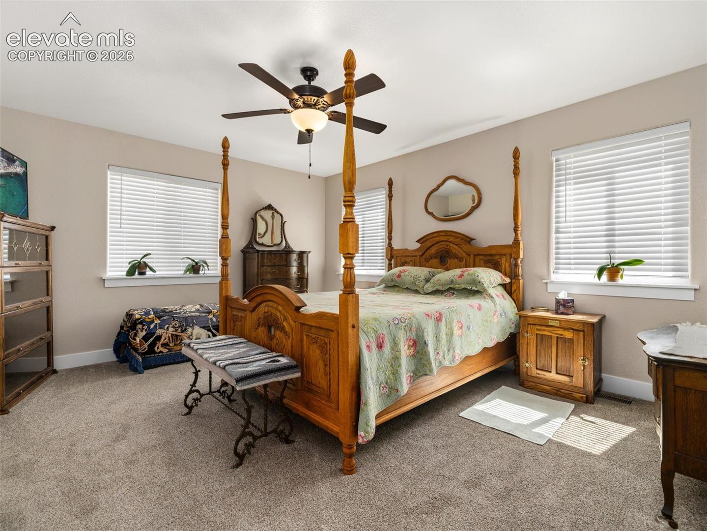 Carpeted bedroom featuring two windows with blinds, a ceiling fan with integrated lighting, and neutral-toned walls