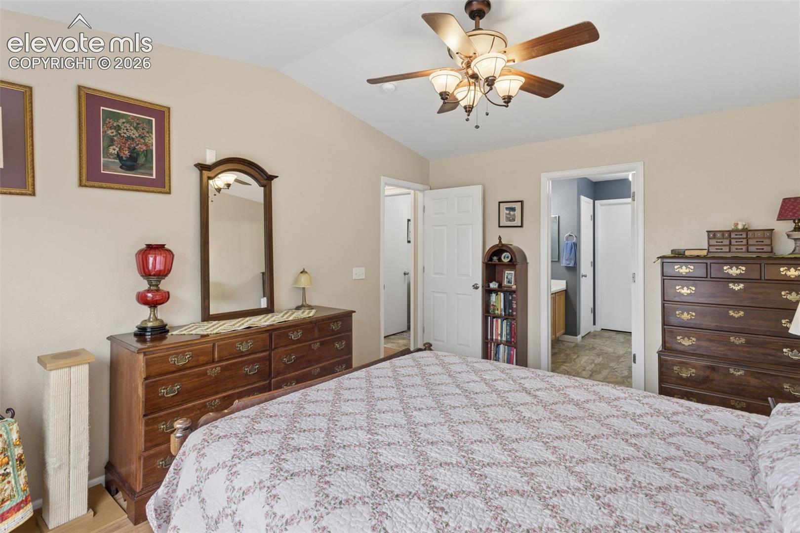 Vaulted ceiling, ceiling fan with integrated lighting, wood-finish flooring, and a full bathroom attached with walk-in closet attached.