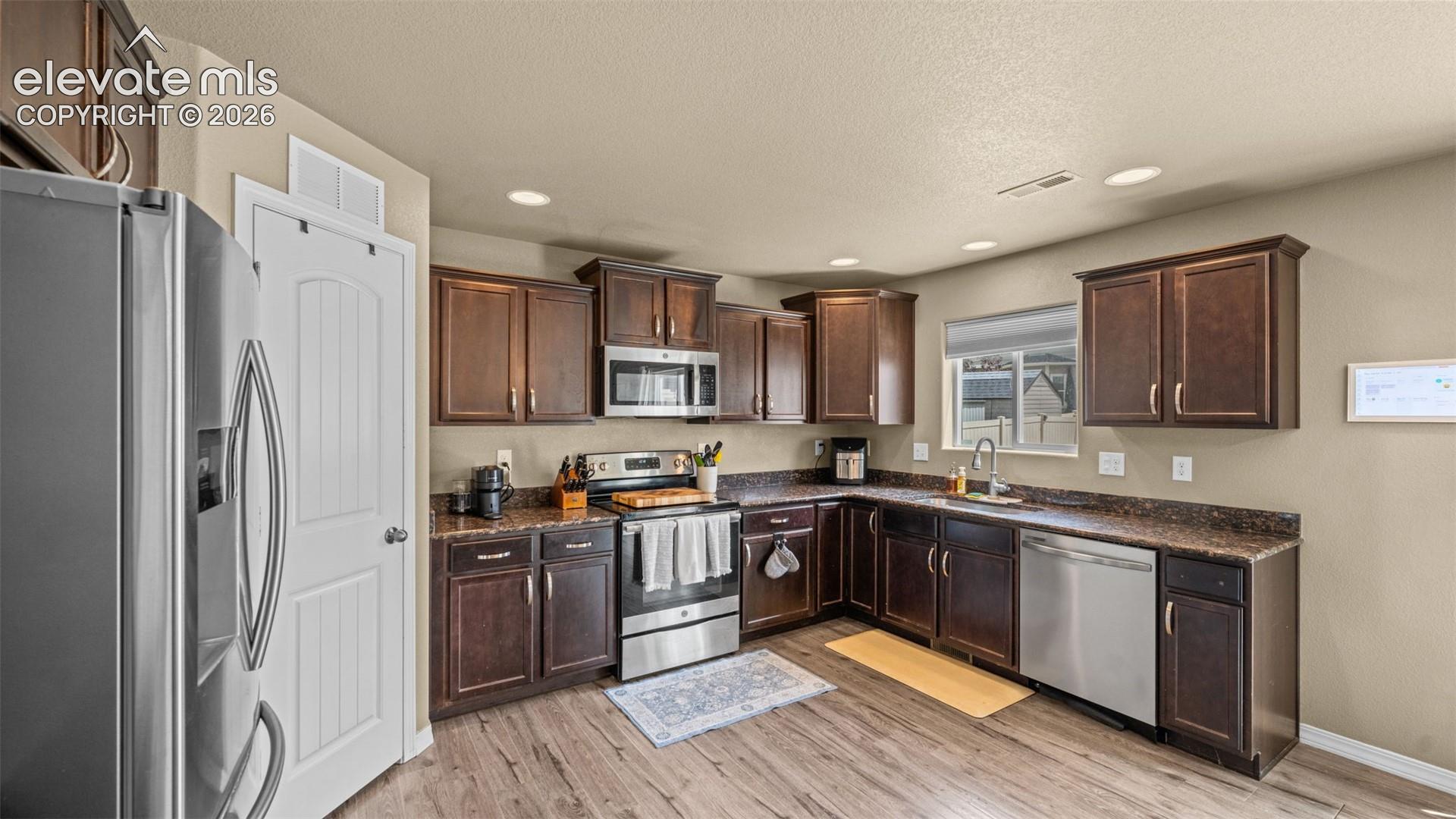 Contemporary kitchen featuring rich wood cabinetry, stainless steel appliances, speckled countertops, and wood-finish flooring