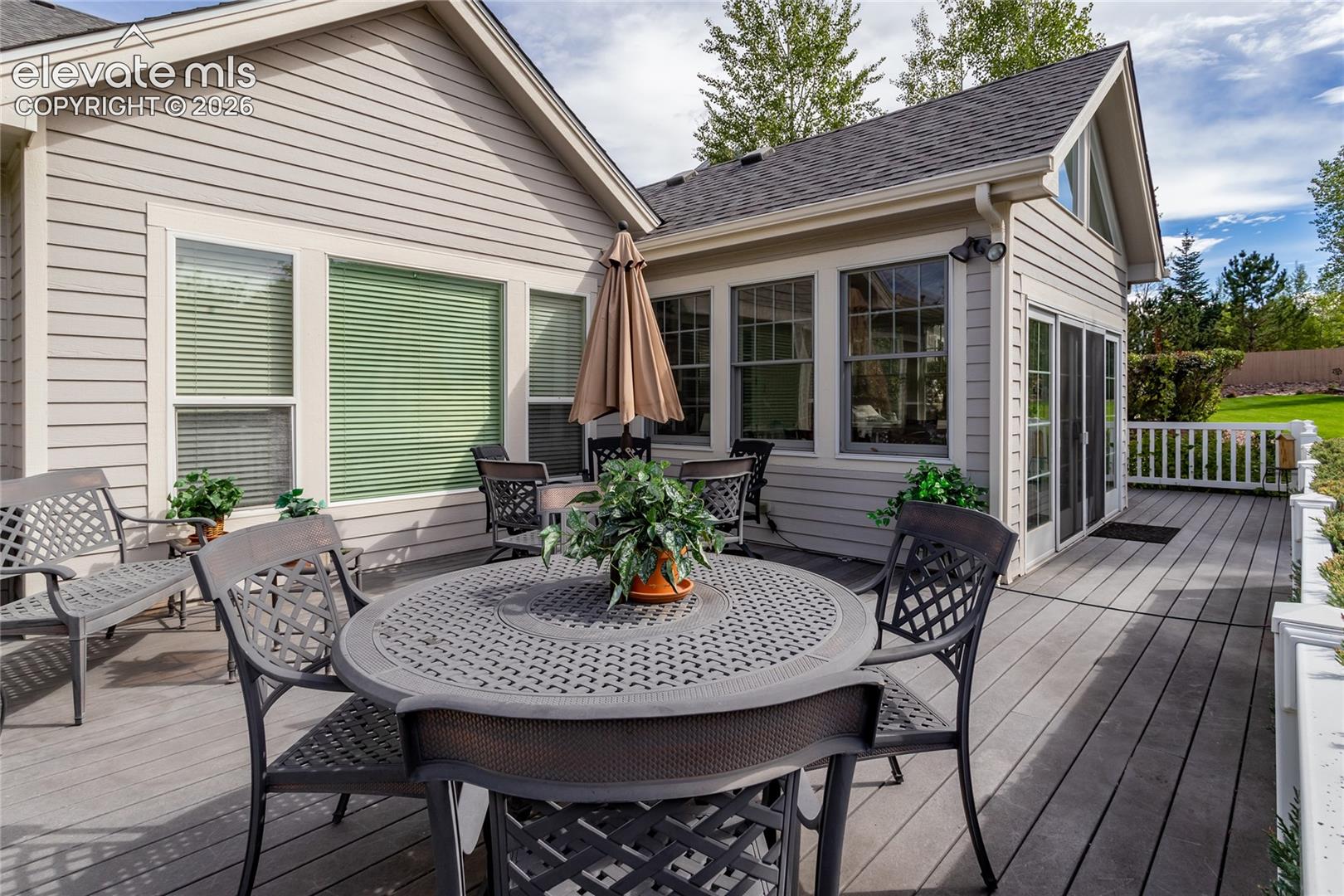 Expansive composite deck featuring a white railing, exterior horizontal siding, multiple grid-pattern windows, and vaulted roofline