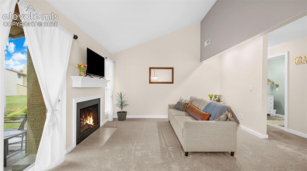 Living area featuring a fireplace with a white mantel, carpeting, and a vaulted ceiling