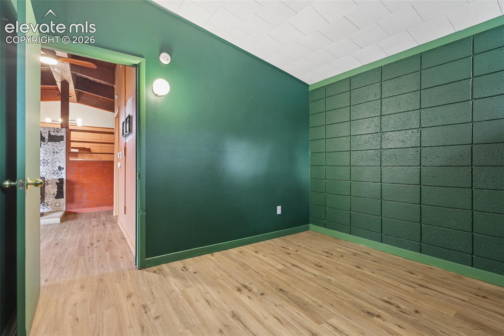 Wood-finish flooring, accent wall with rectangular block texture, smooth painted walls, and textured ceiling panels