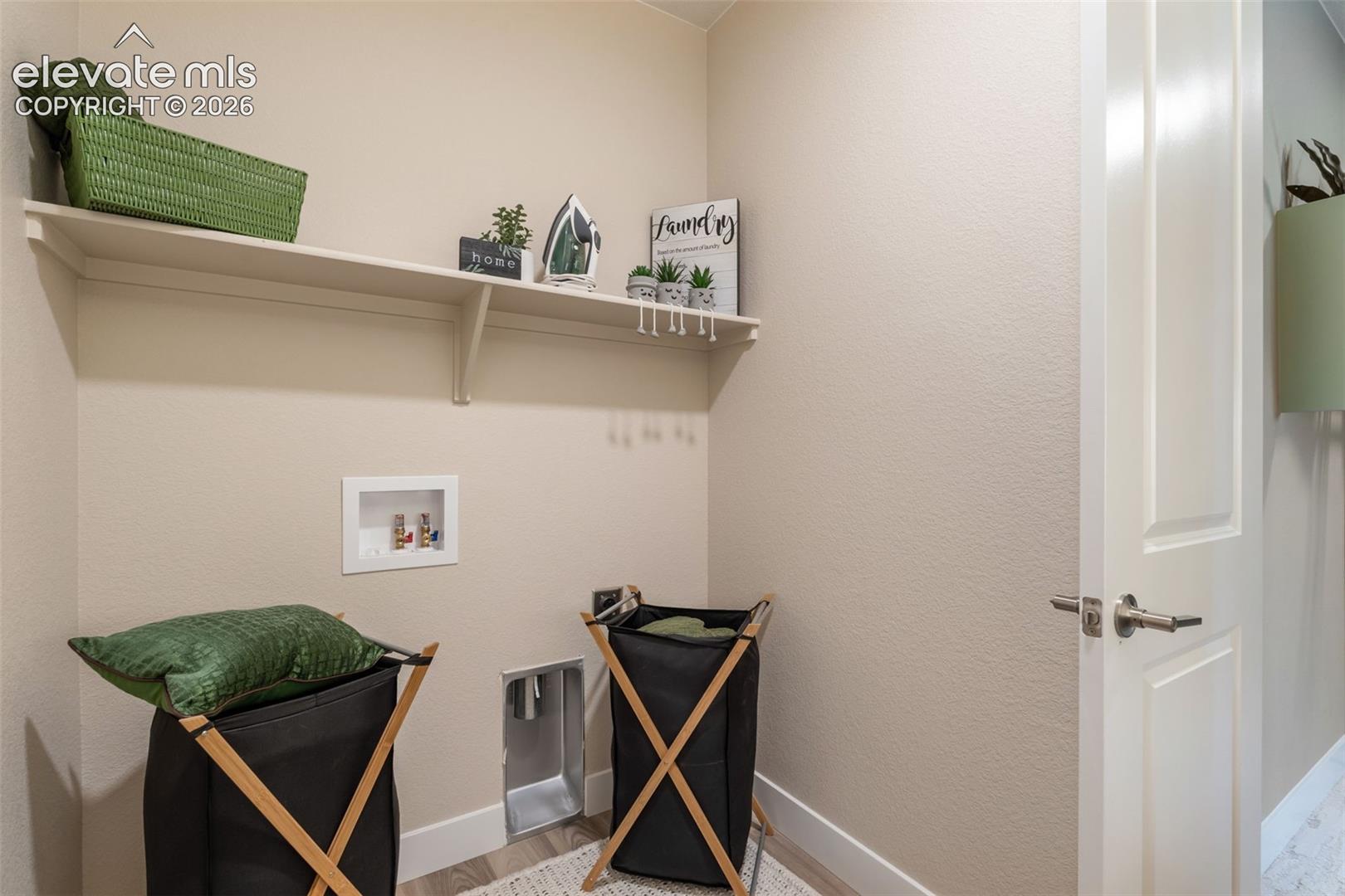 Dedicated utility space featuring a wall-mounted storage shelf and recessed plumbing hookups