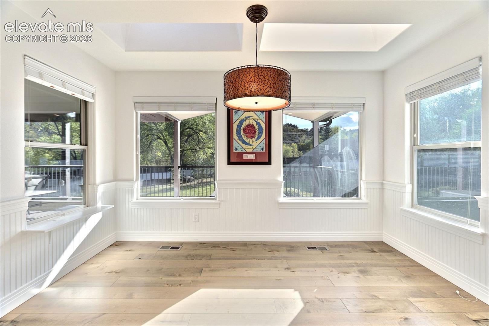 Bright room featuring wood-finish flooring, white beadboard wainscoting, dual skylights, and a tiered drum pendant light