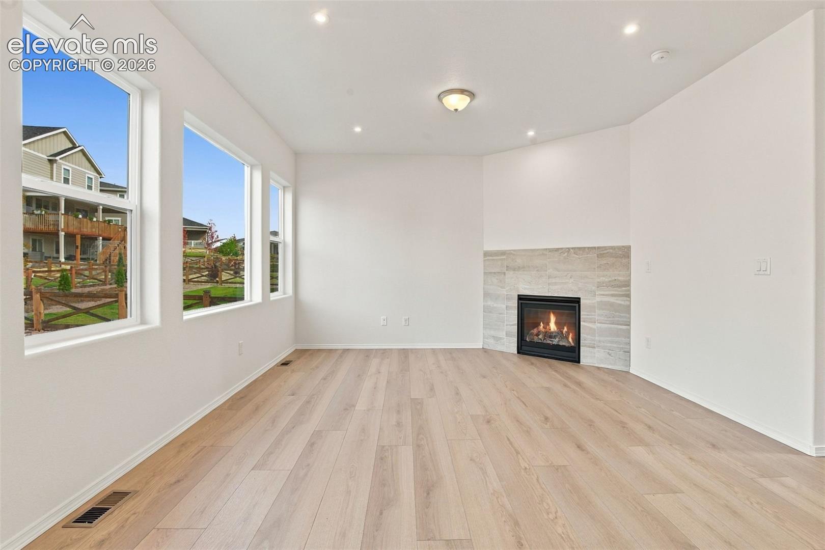 Interior space featuring wood-finish flooring, recessed lighting, and a corner fireplace with a horizontal stone-tile surround, accented by large picture windows