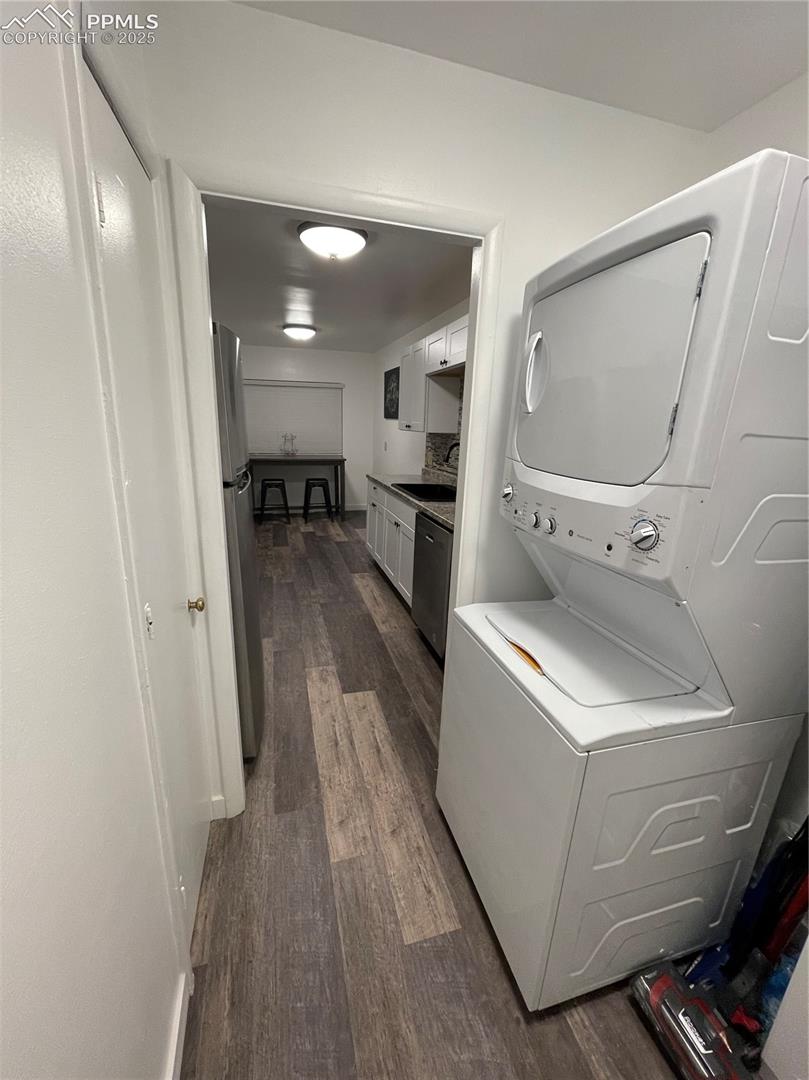 Laundry area with stacked washing machine and dryer and dark wood-style flooring