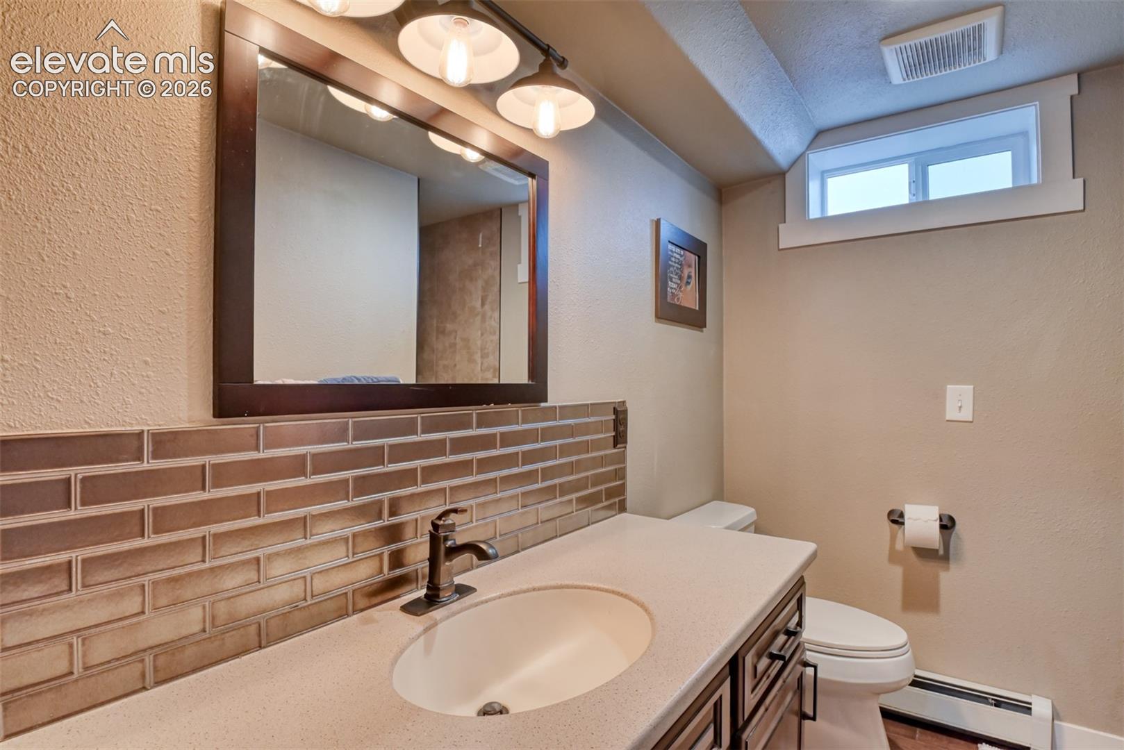 Bathroom featuring vanity, a baseboard heating unit, a textured wall, tasteful backsplash, and a textured ceiling