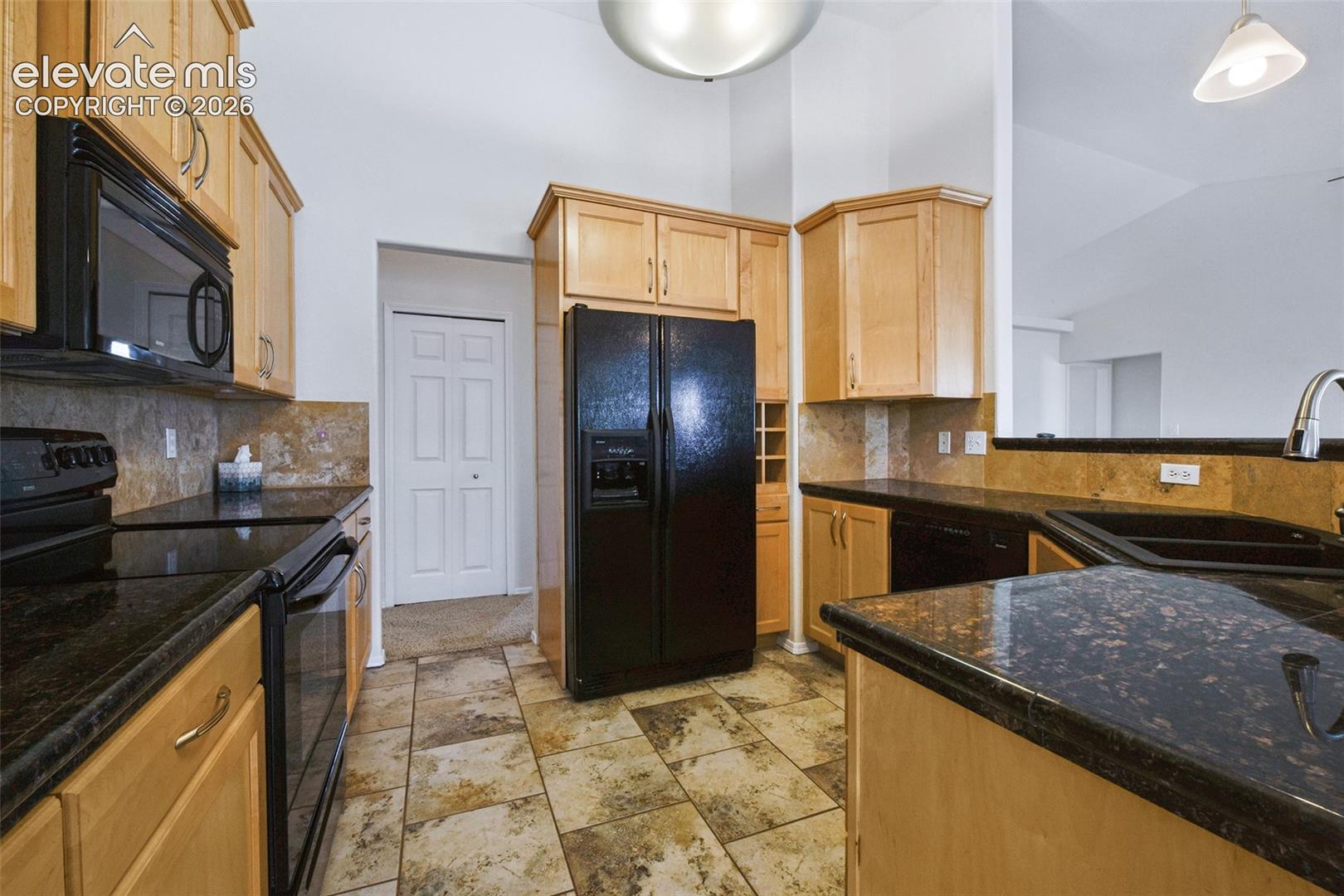 Kitchen featuring dark countertops, light wood-finish cabinetry, black appliances, and tile flooring