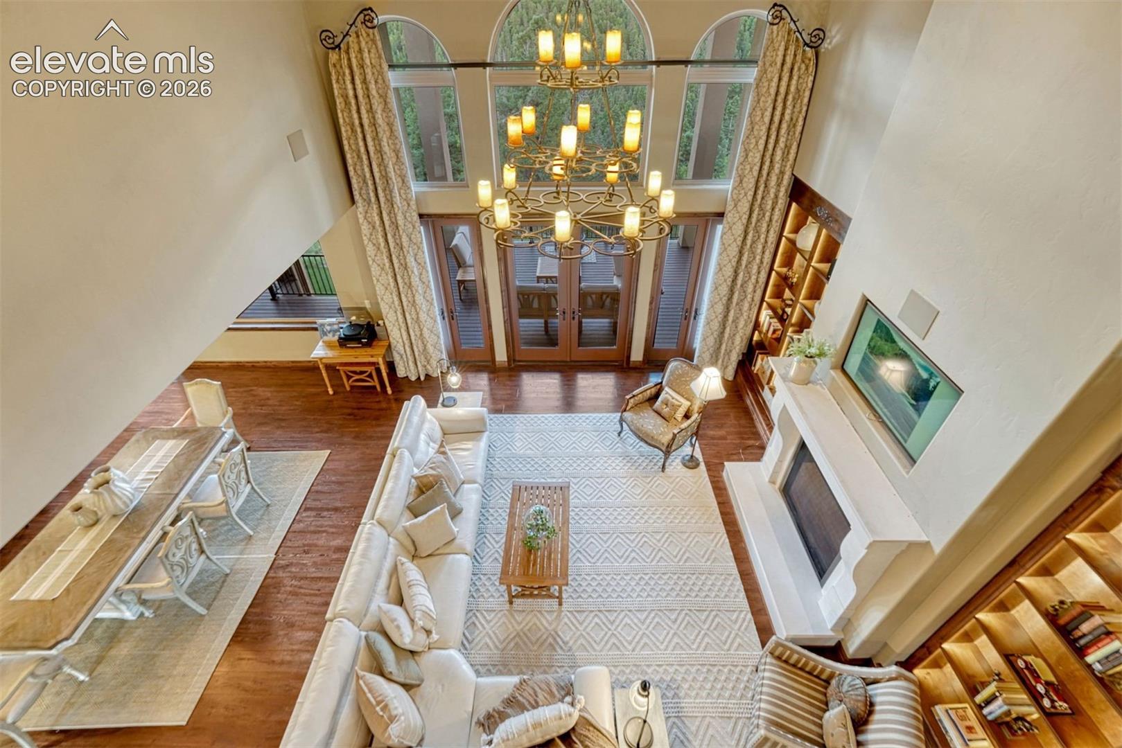 Spacious living area featuring a prominent chandelier, arched windows with exterior access, a built-in fireplace, and integrated shelving