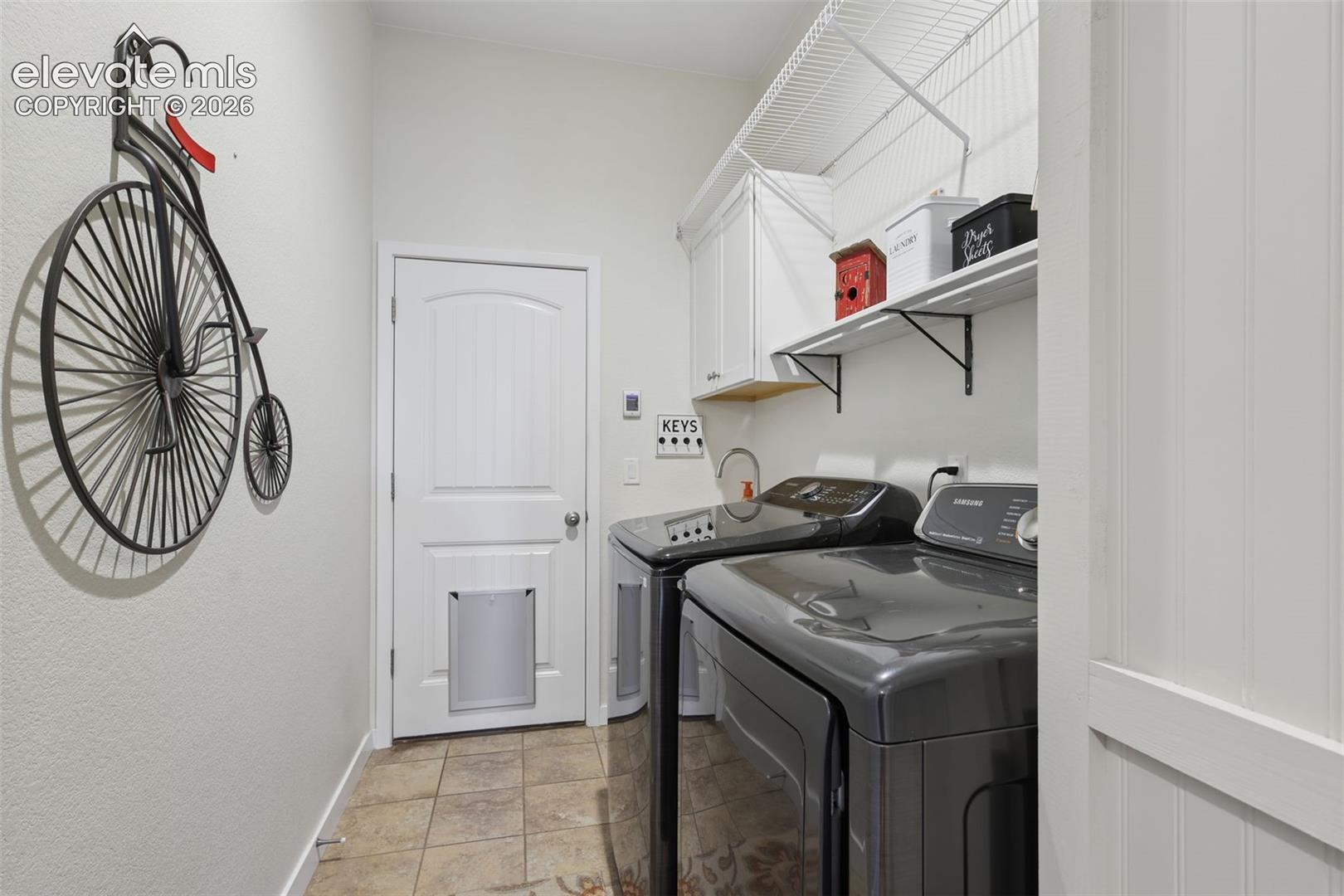 Laundry space featuring tile flooring, white cabinetry, integrated shelving, and a paneled door