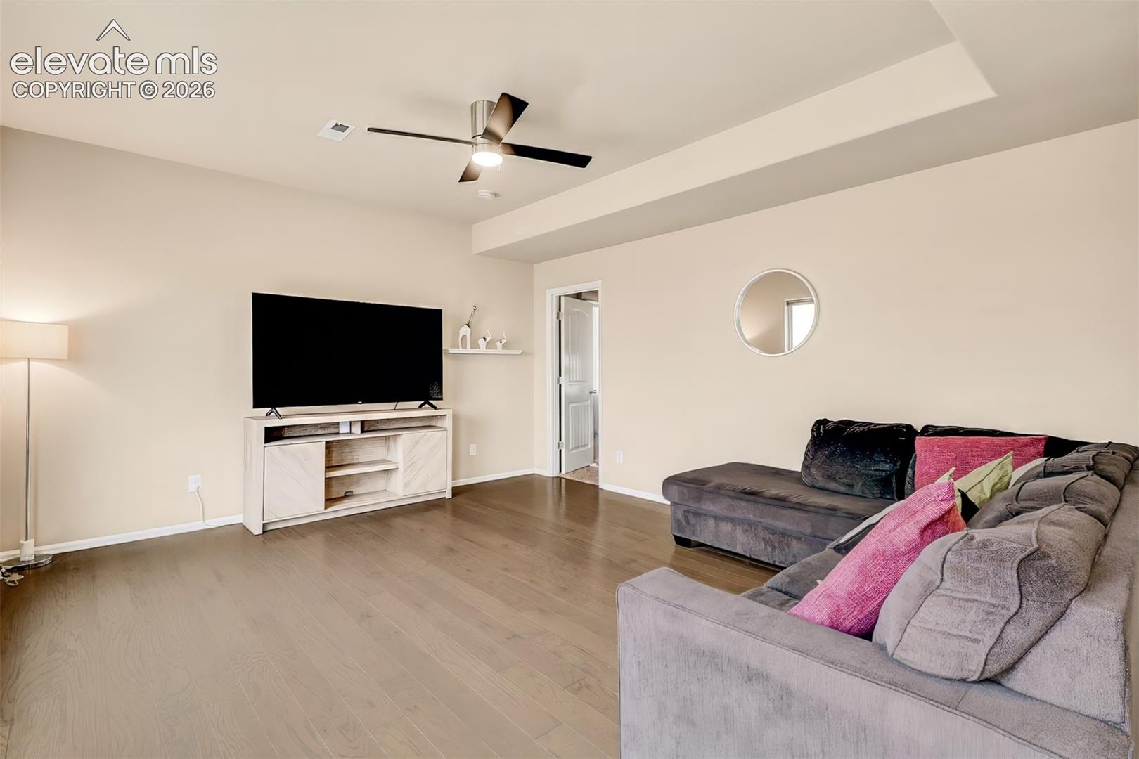 Living area featuring wood-finish flooring, recessed tray ceiling, and a central ceiling fan