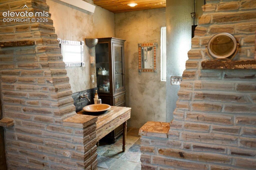 Stone-clad interior walls featuring a wooden vanity with a vessel sink