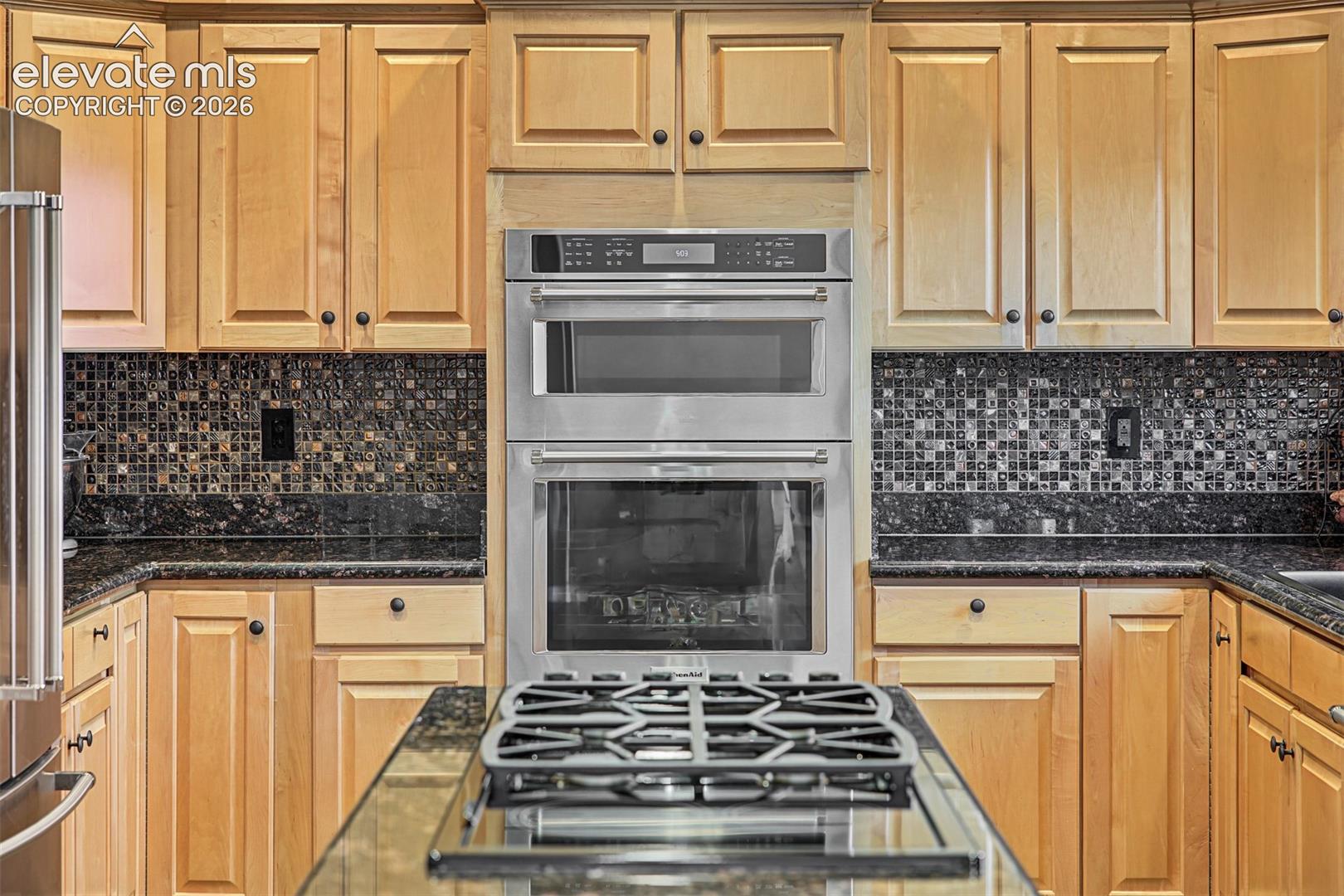 Spacious kitchen featuring warm wood cabinetry, granite countertops, tile backsplash, center island with gas cooktop, double wall ovens, and recessed lighting.