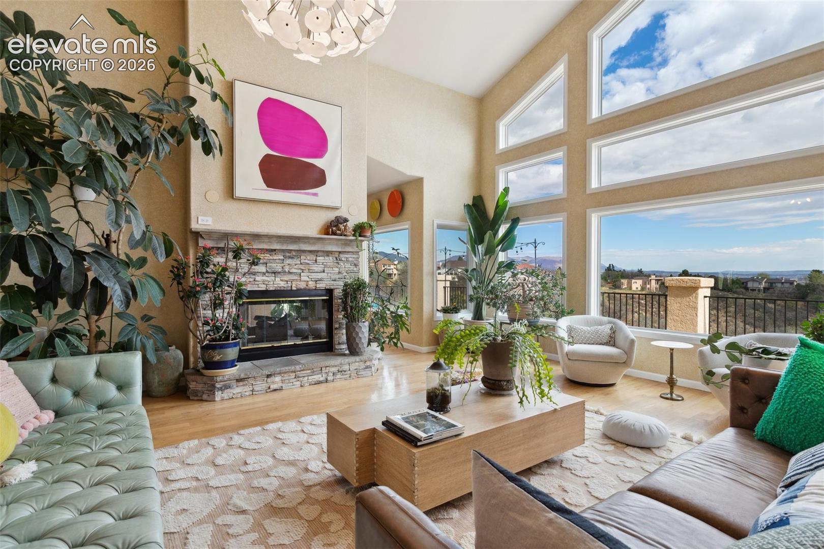 Vaulted ceiling living space featuring a stone fireplace, wood-finish flooring, and expansive windows