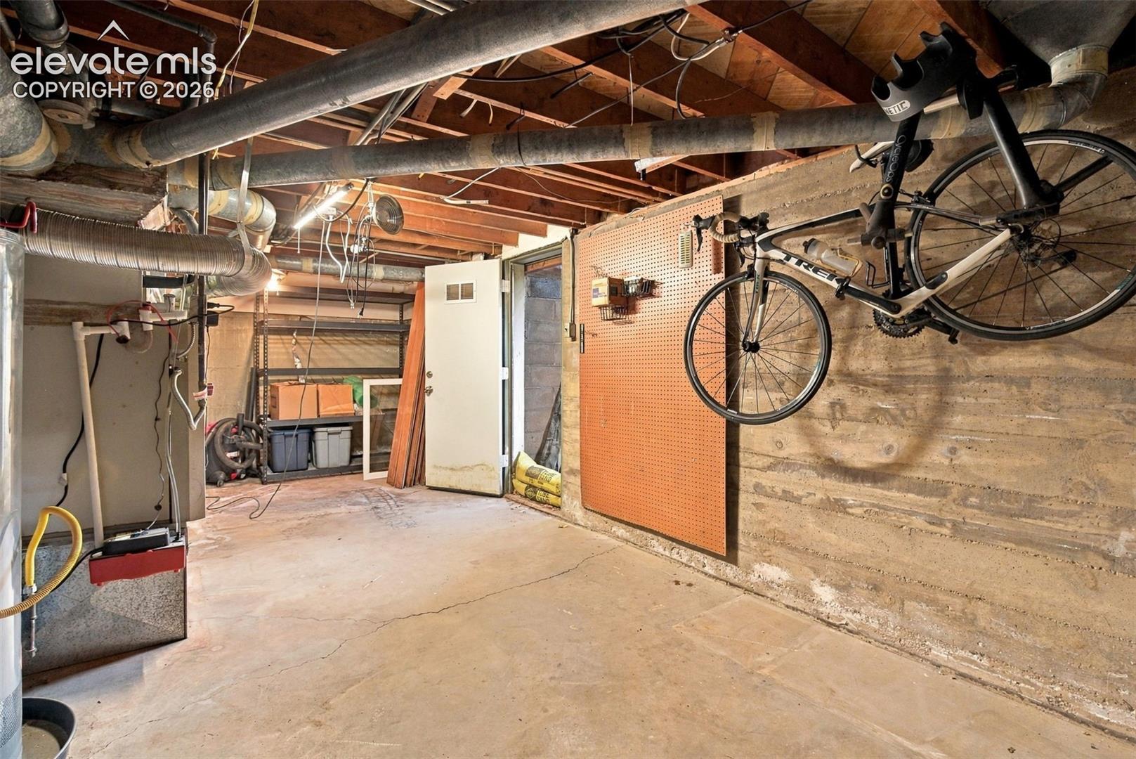 Unfinished lower level featuring exposed wood-joist ceiling, concrete floor, concrete foundation walls, and an exterior access door