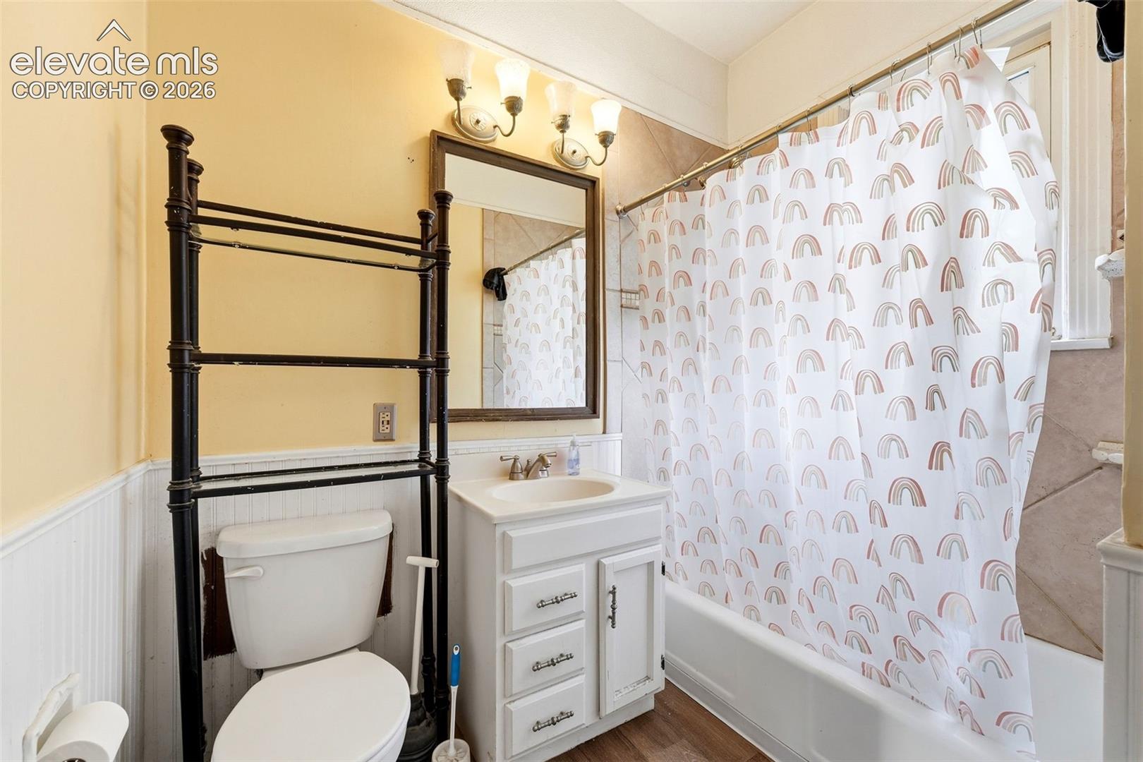 White vanity with integrated sink, wood-finish flooring, a white bathtub, and a built-in toilet