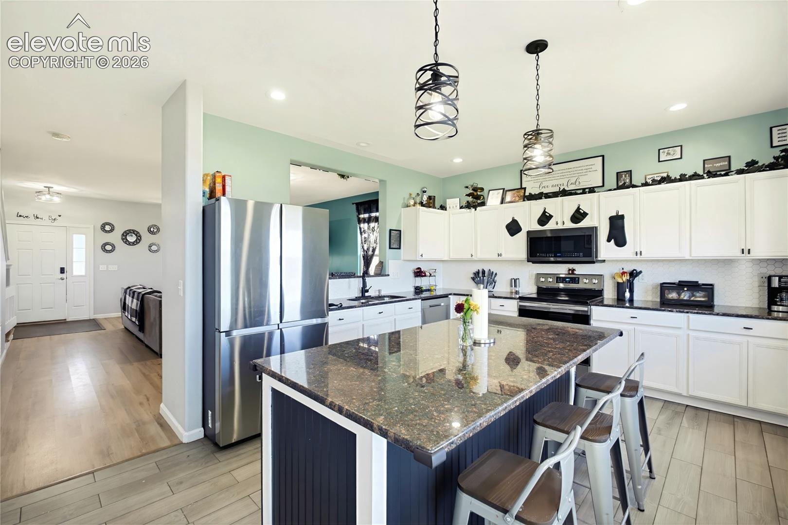Kitchen featuring white cabinetry, dark countertops, stainless steel appliances, and a central island with bar seating