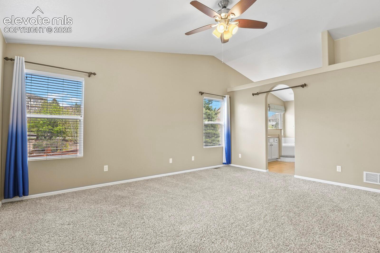 Spacious room featuring vaulted ceilings, light tan walls, and wall-to-wall carpeting