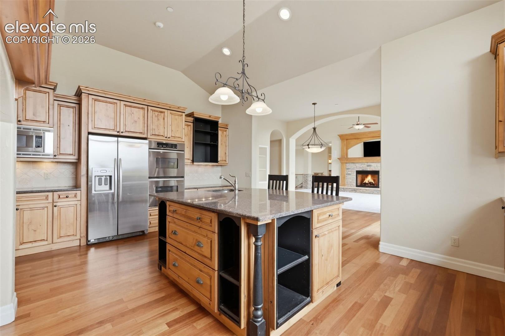 Spacious kitchen featuring an expansive center island with seating, stainless steel appliances, light wood cabinetry, and wood-finish flooring