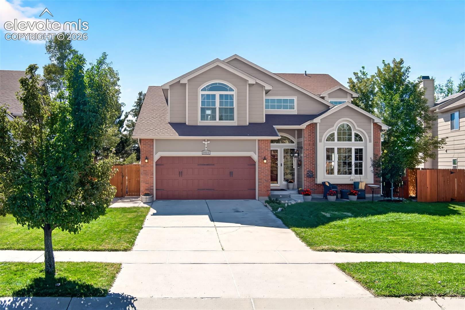 Two-story home with brick accents, arched windows, and a red double garage door.