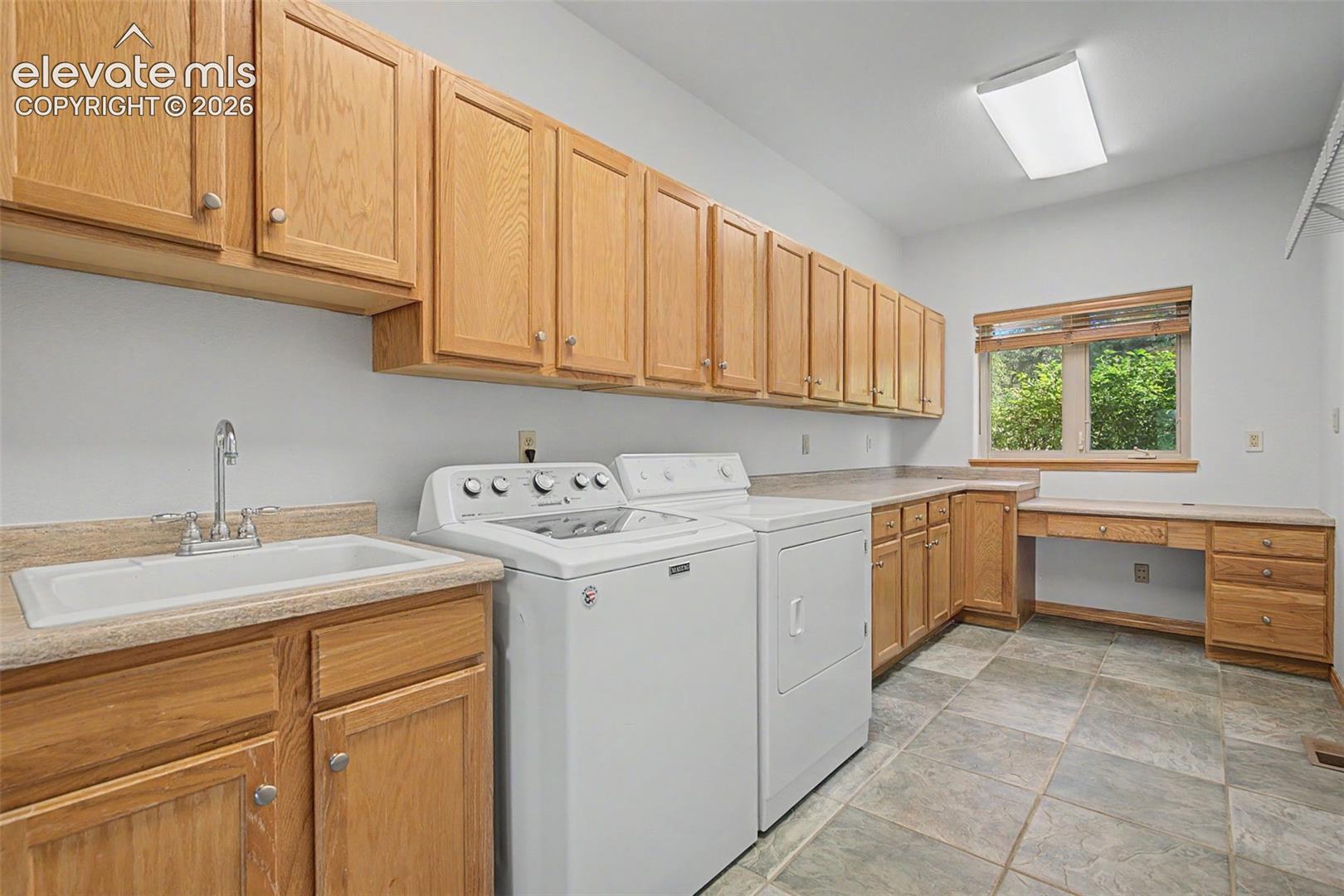 Spacious utility room featuring extensive natural wood cabinetry, a built-in workstation, a utility sink, and tile flooring