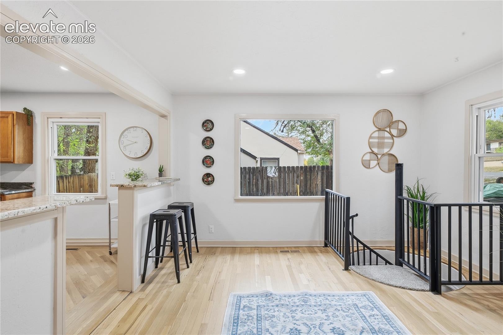 Light-toned wood-finish flooring, breakfast bar with stone-finish countertop, recessed lighting, and black metal staircase railing