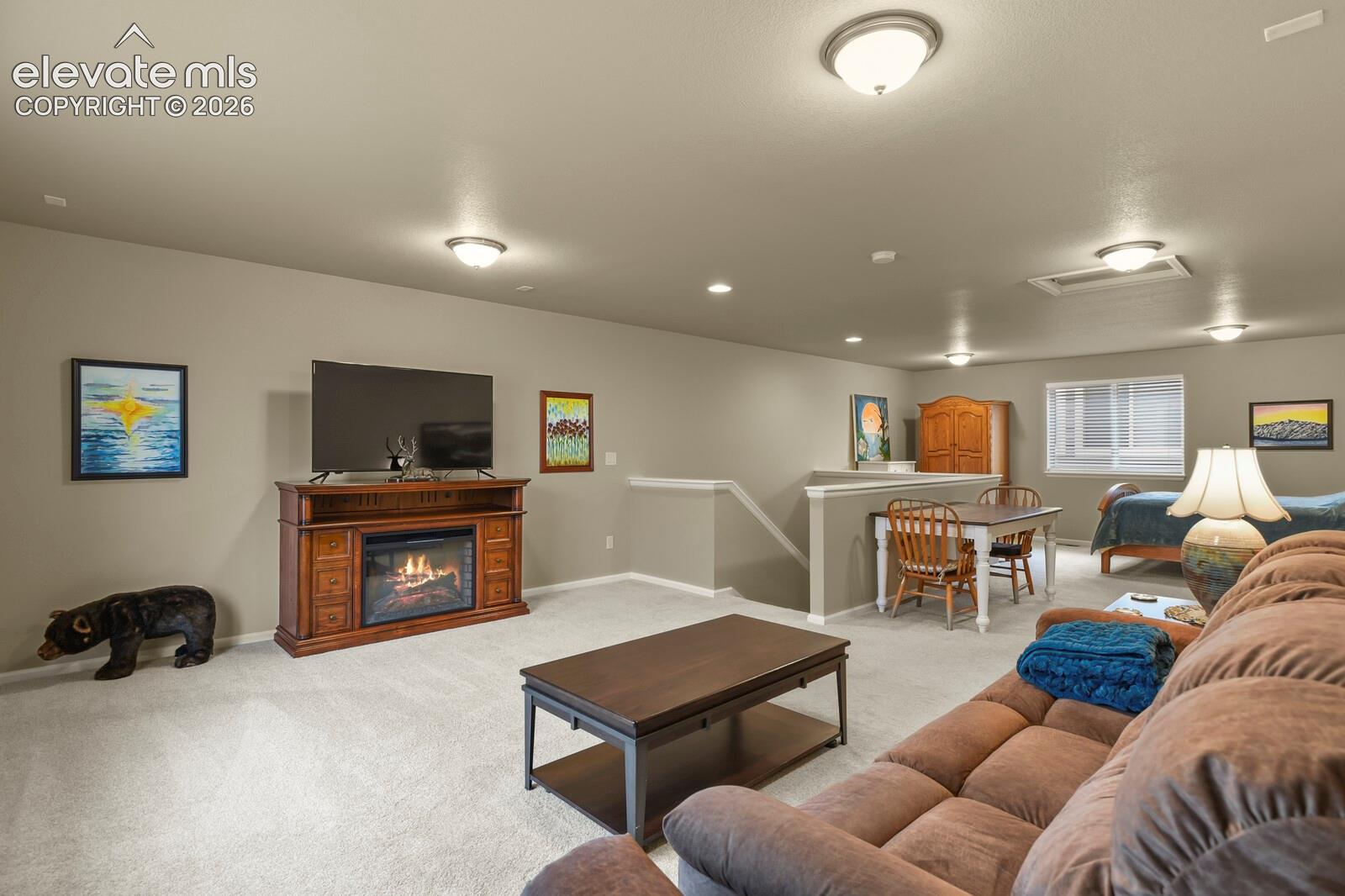 Neutral-toned living space featuring wall-to-wall carpeting, recessed and flush-mount lighting, and a prominent staircase railing.  Easily repurposed for Gym, game Area, Media Room, Etc.