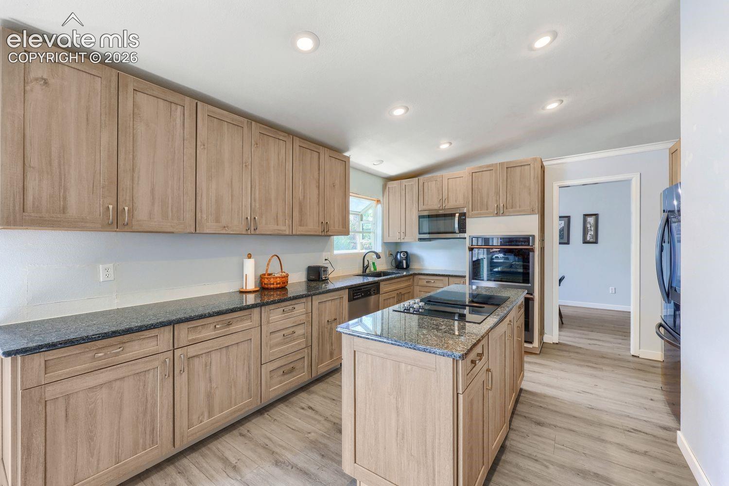 Kitchen featuring wood-finish cabinetry, dark countertops, a center island with cooktop, built-in double ovens, and recessed lighting