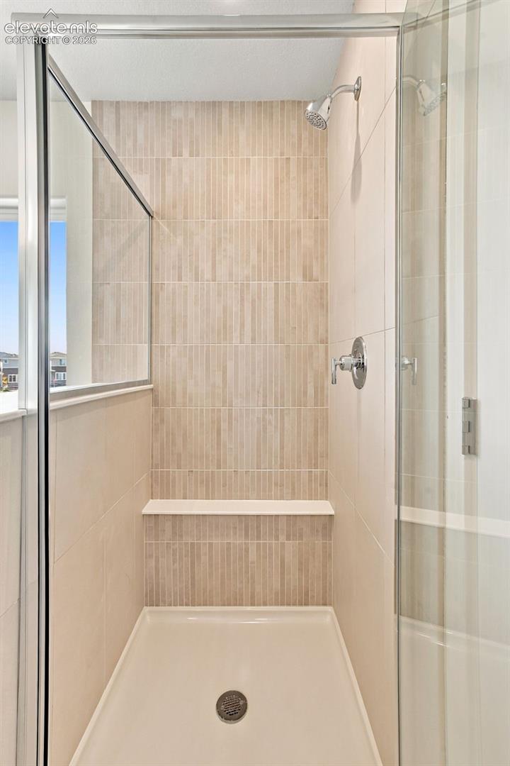 Glass-enclosed shower with a built-in bench, vertical subway tile accent, and chrome fixtures