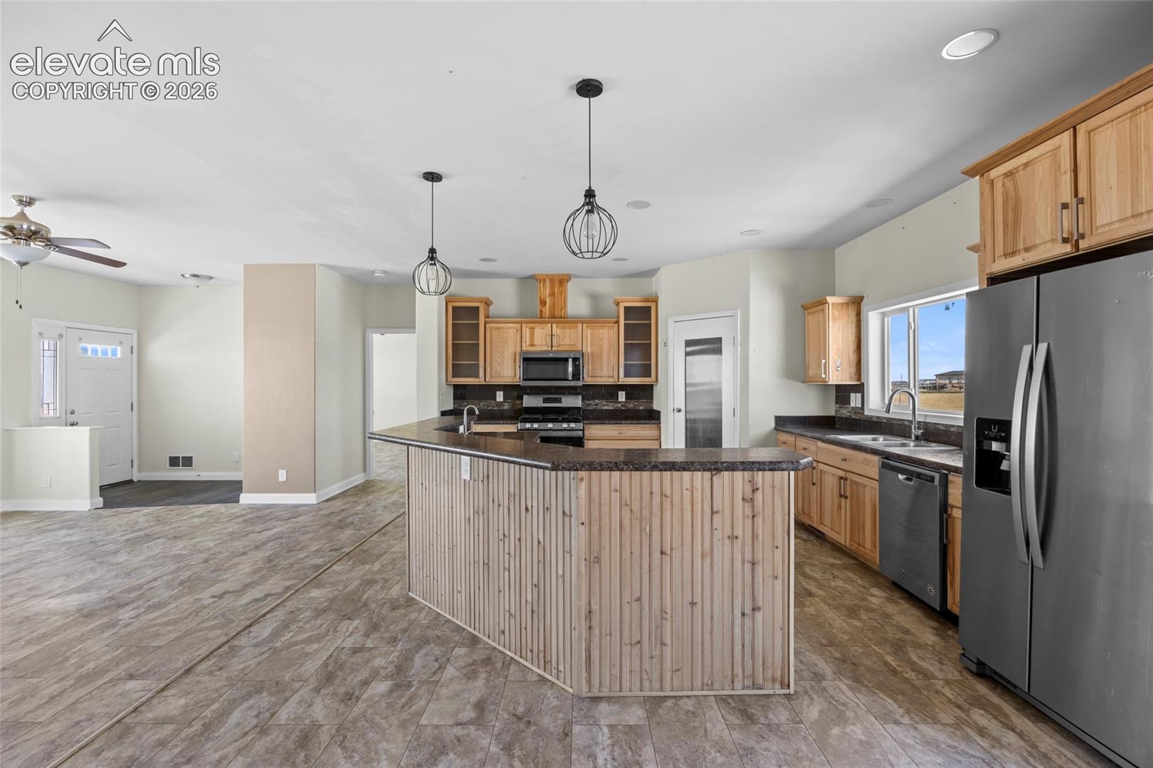 Kitchen featuring natural wood cabinetry, stone-finish countertops, stainless steel appliances, beadboard island detailing, and pendant lighting