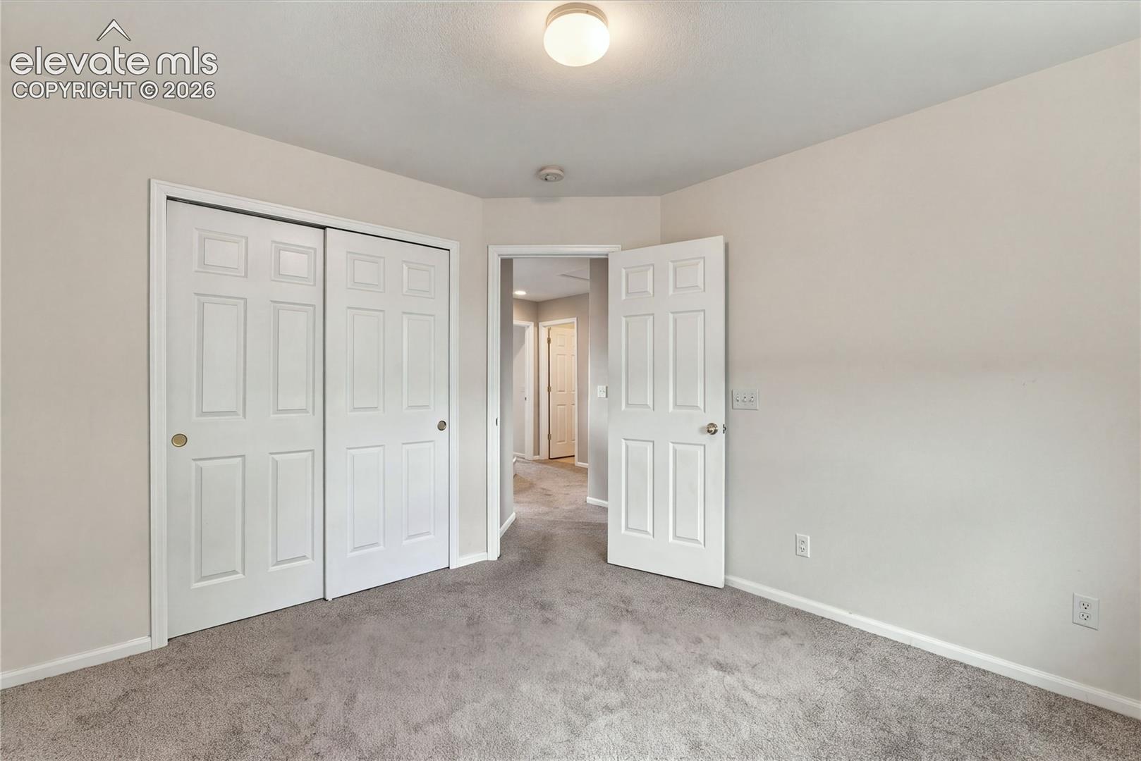 Neutral-toned wall-to-wall carpeting, six-panel closet doors, and flush-mount overhead lighting