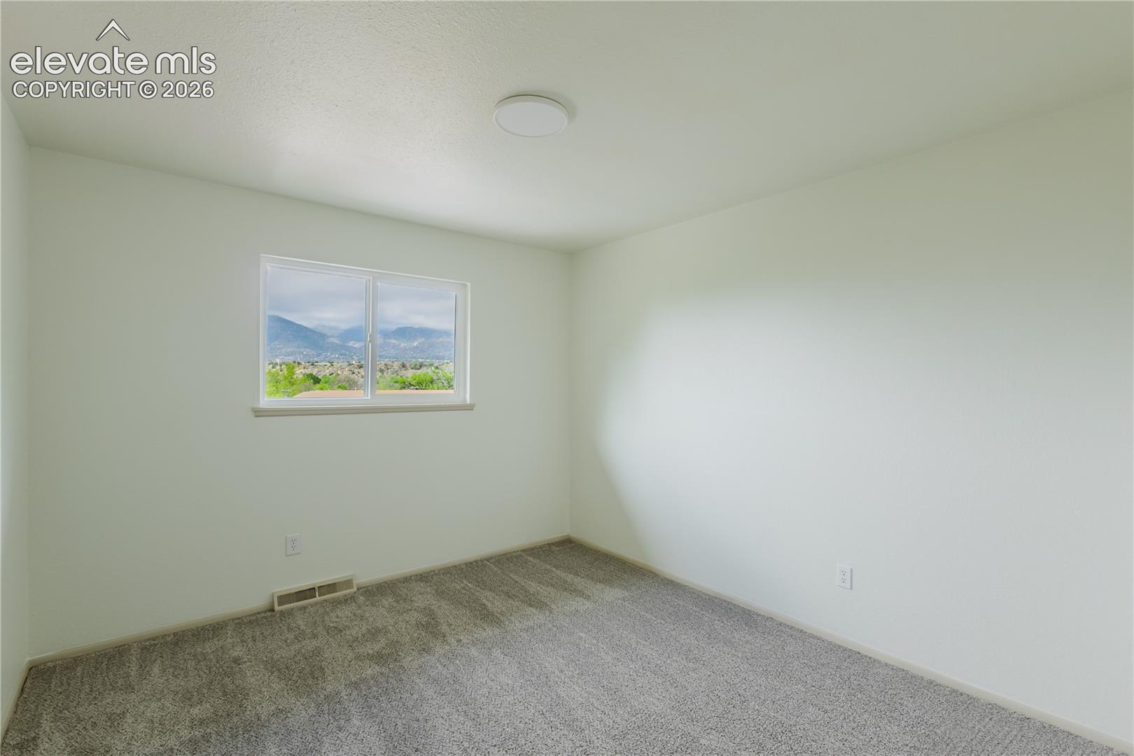 3rd bedroom - Bright interior space featuring a window with a distant mountain backdrop, light gray carpeting, and white walls
