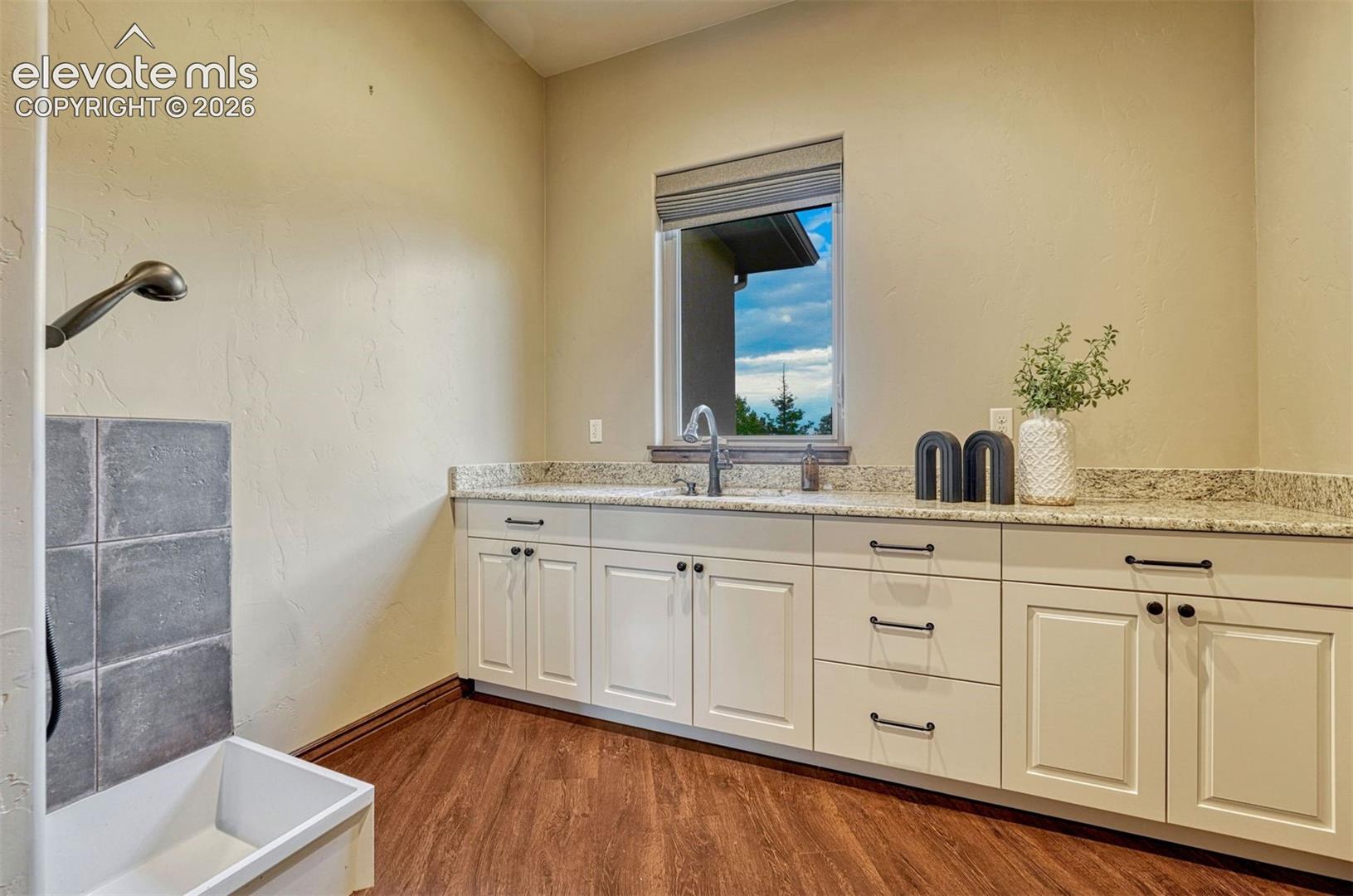 Built-in cabinetry with granite-finish countertops, undermount sink, a large window, and wood-finish flooring