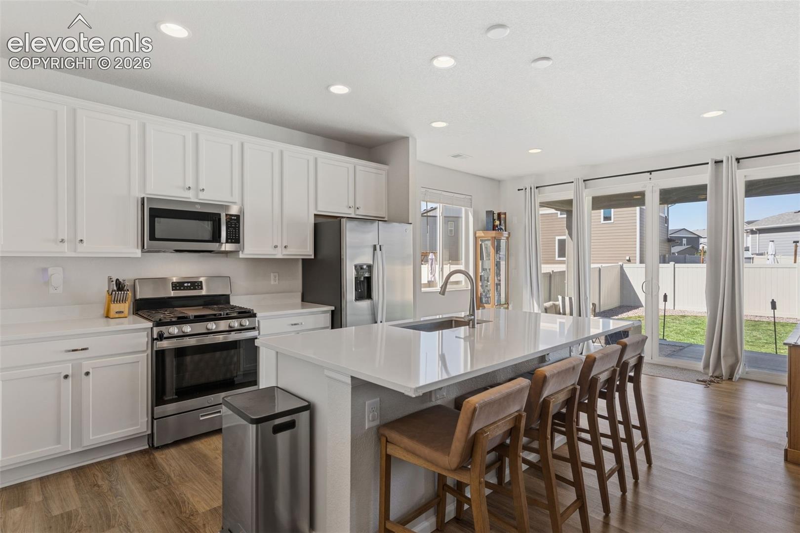 Contemporary kitchen featuring a large center island with integrated sink, white cabinetry, stainless steel appliances, and wood-finish flooring