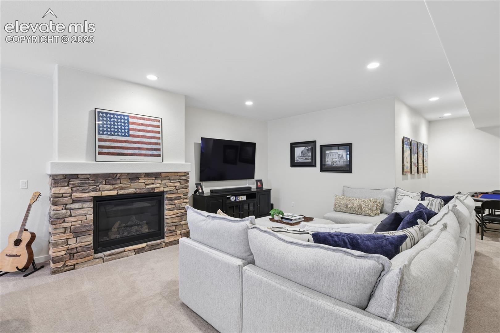 Finished basement recreation room featuring a stone-surround fireplace with gas insert, recessed lighting throughout, and neutral carpeting
