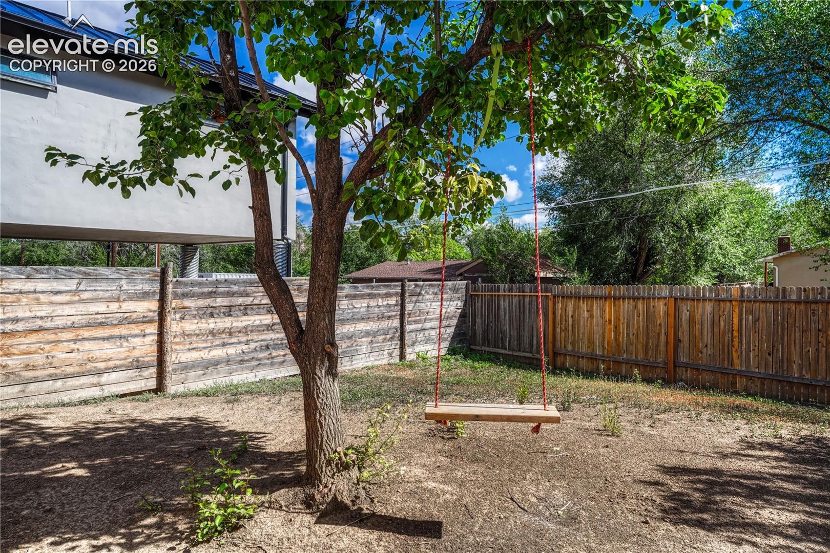 Expansive backyard with a mature tree, wood plank fencing, and partial stucco exterior