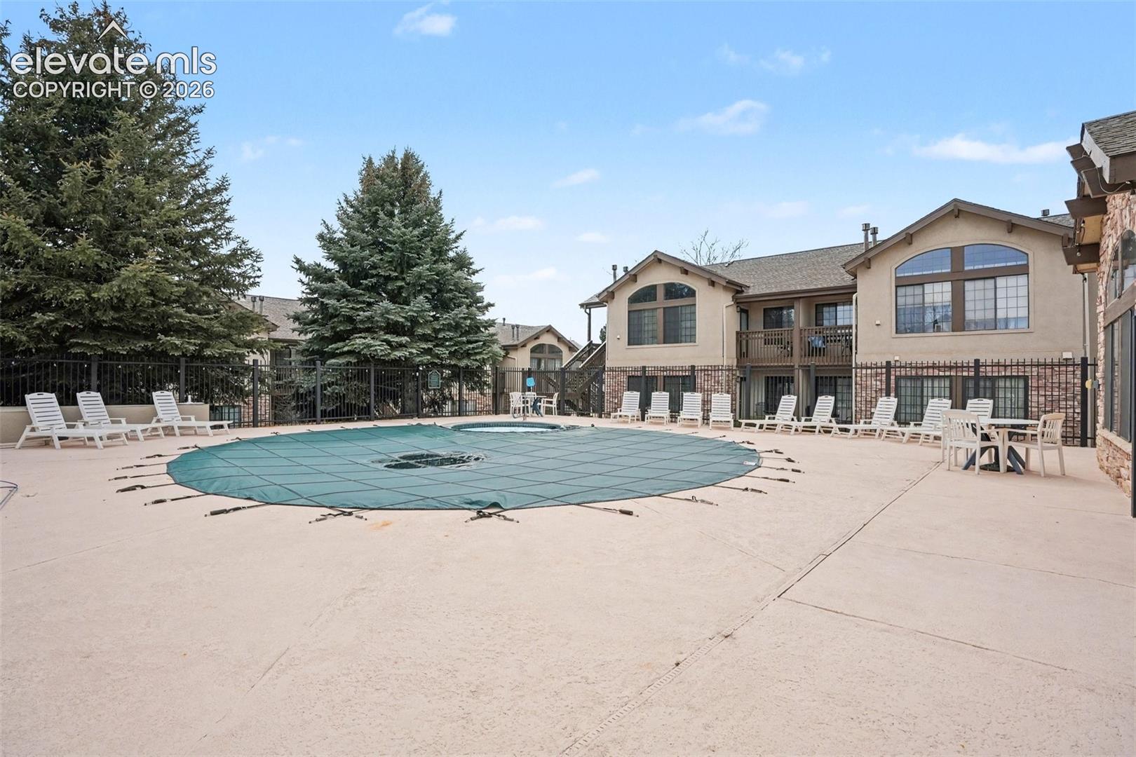 Community swimming pool with a hardscape patio, stone-veneer exterior building accents, arched window detailing, and metal perimeter fencing