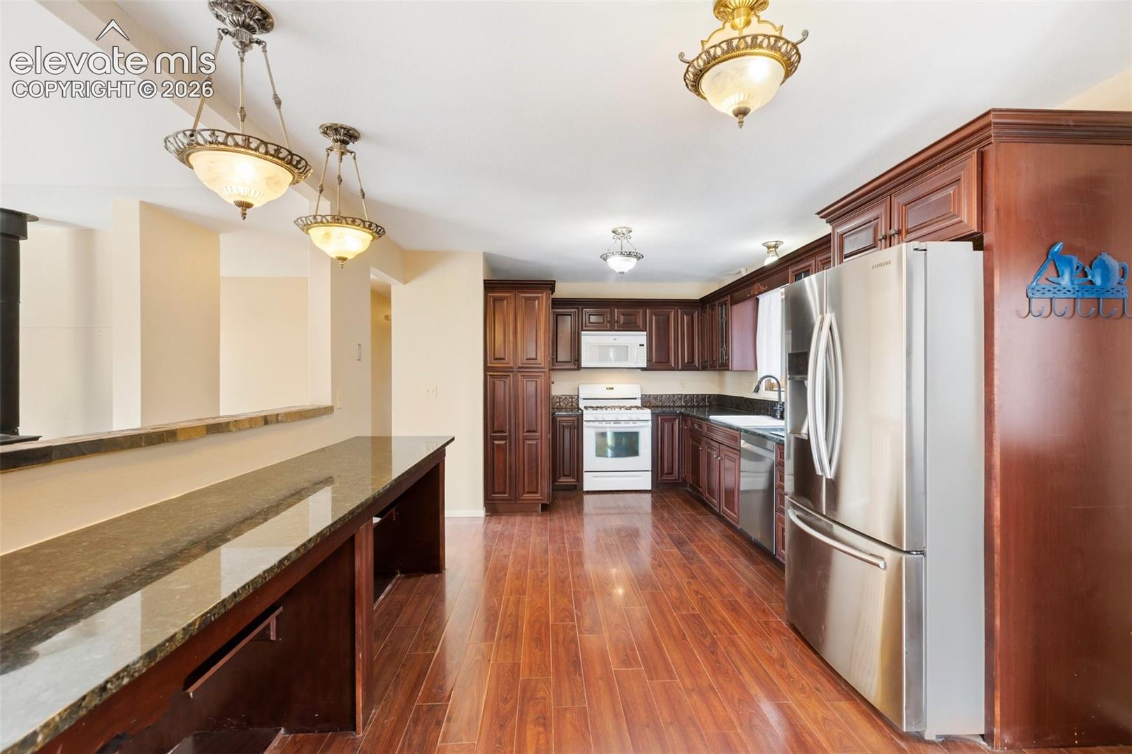 Kitchen featuring dark wood-finish cabinetry, stainless steel refrigerator, white microwave, white range, and wood-finish flooring