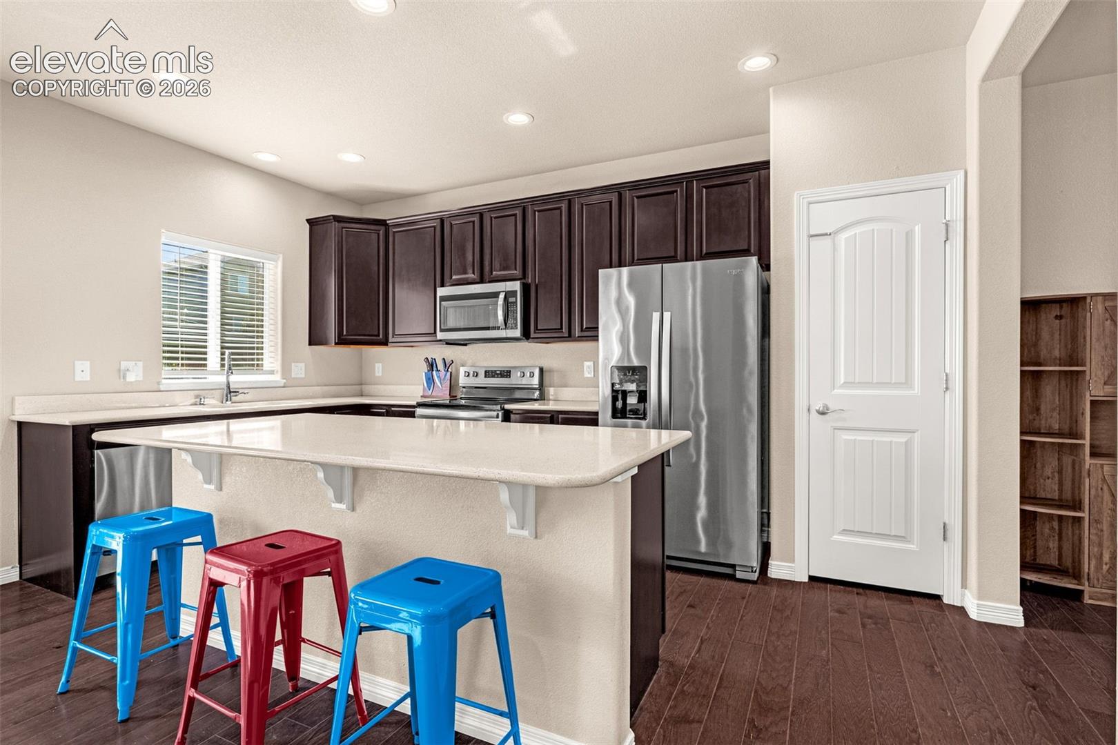 Kitchen featuring wood-finish flooring, recessed lighting, dark wood cabinetry, stainless steel appliances, and a built-in breakfast bar