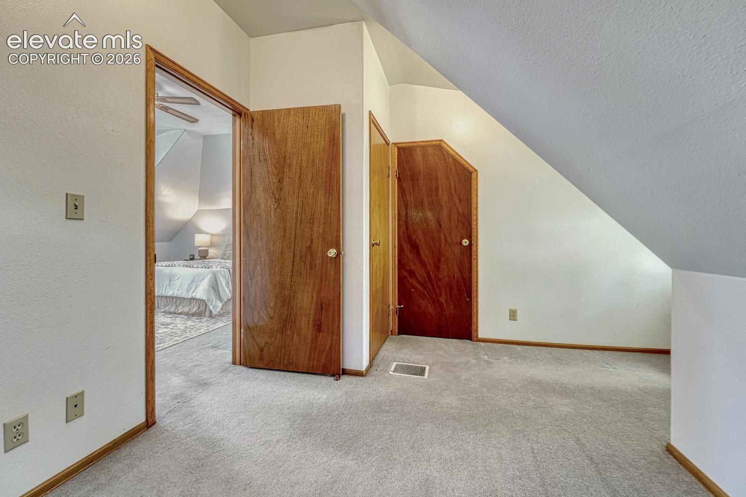 Carpeted flooring, wood-finish doors, white walls, and sloped ceiling