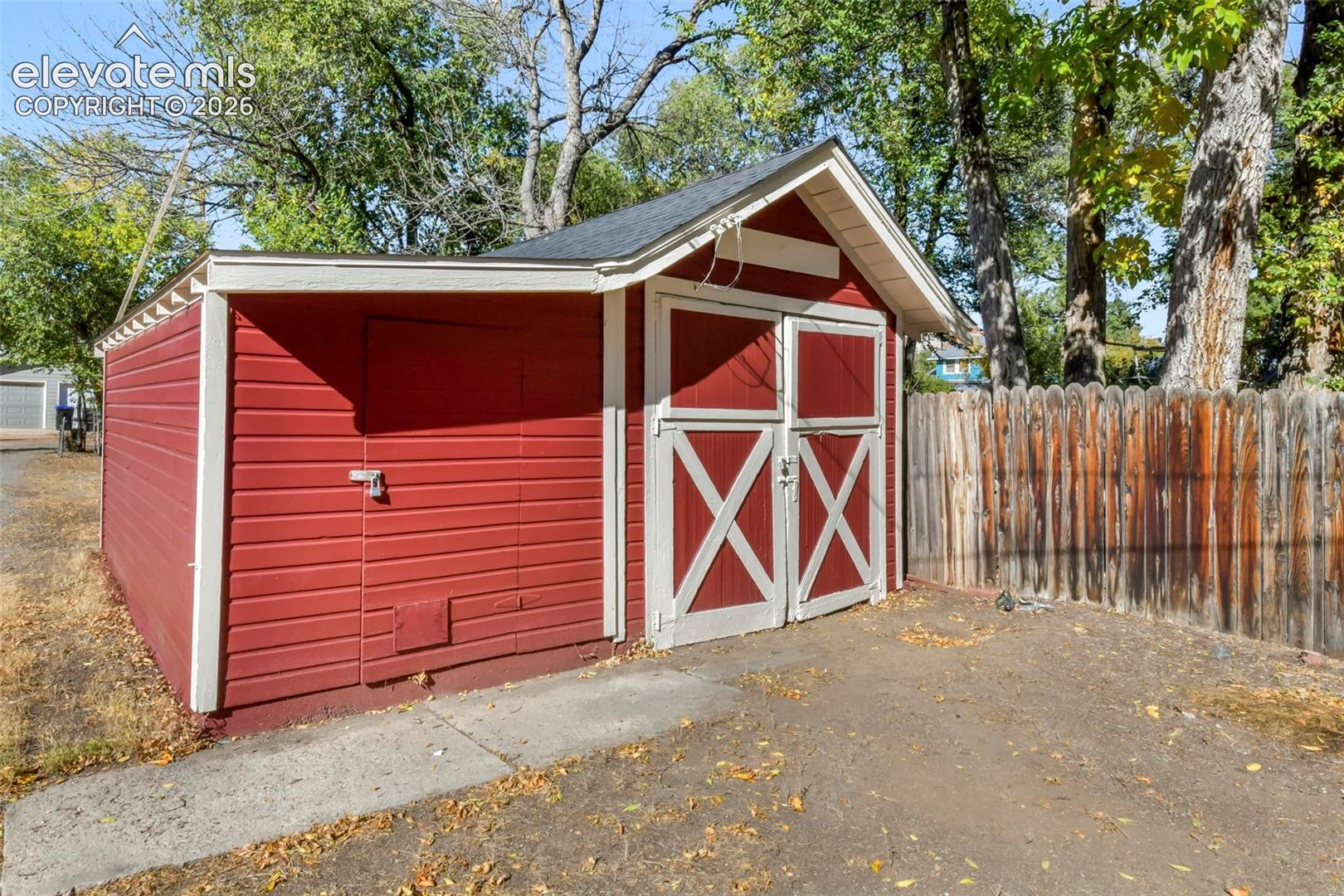 Detached storage structure featuring red wood siding, white trim, a gable roof, and double barn-style doors