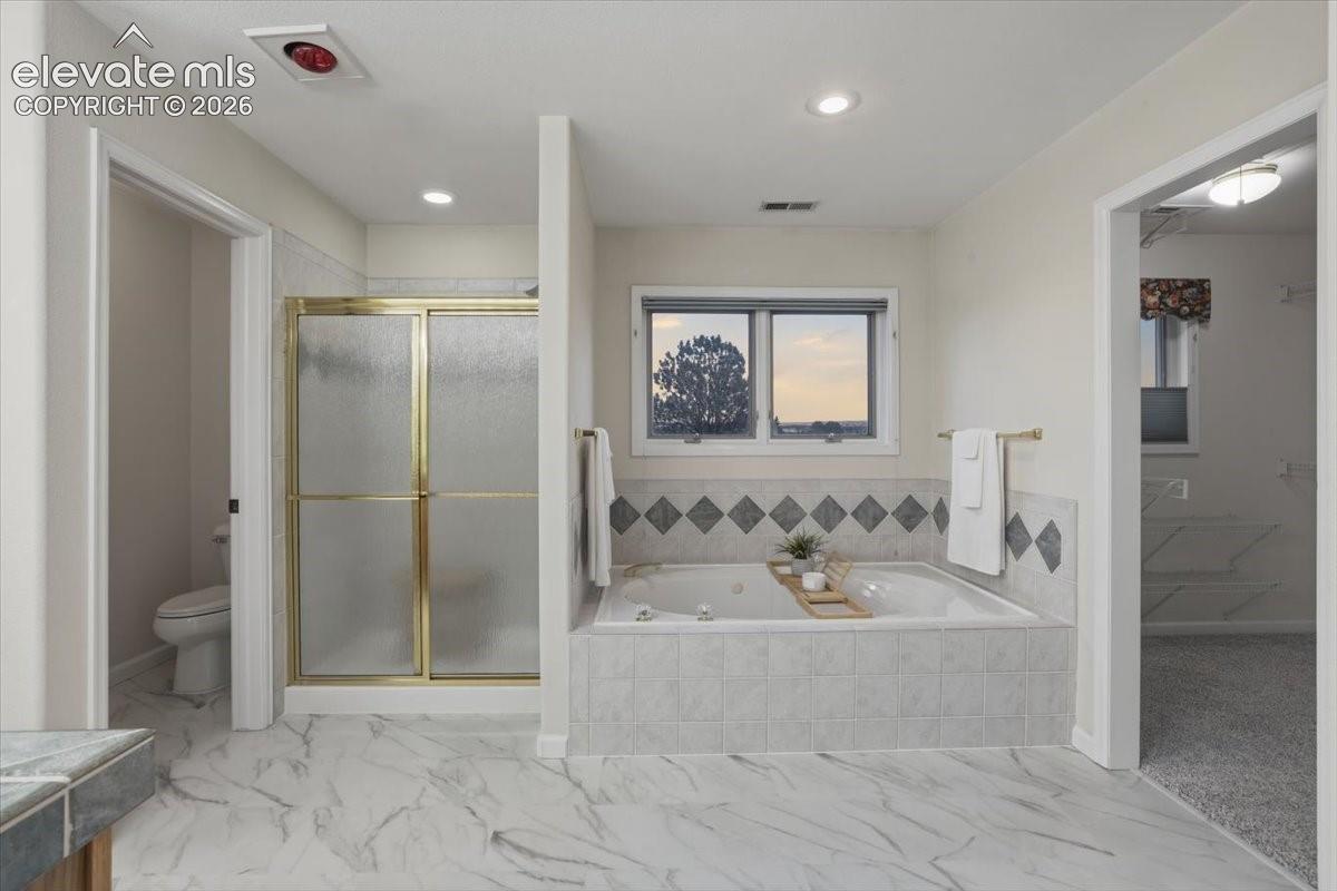 Tiled flooring extending throughout, built-in soaking tub with tiled surround, and a shower enclosure with frosted glass doors