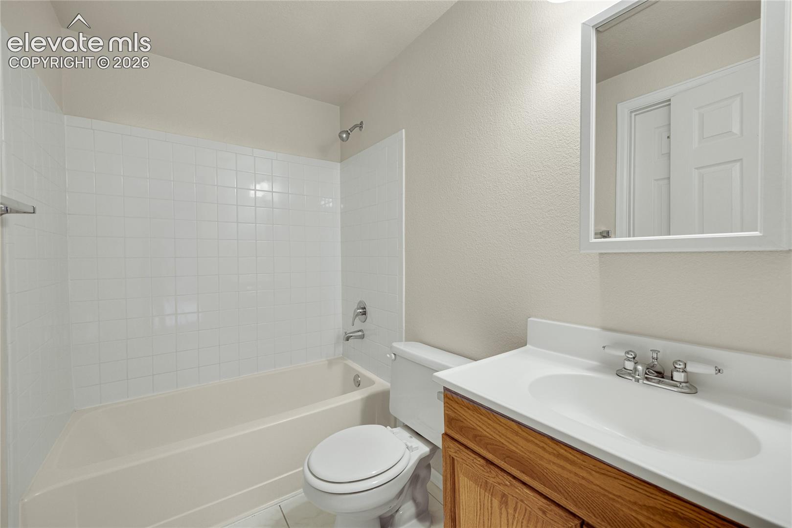 Full bathroom featuring a vanity with a white countertop and oval basin, wood-finish cabinetry, a framed wall mirror, and a tub-shower combination with white tile surround