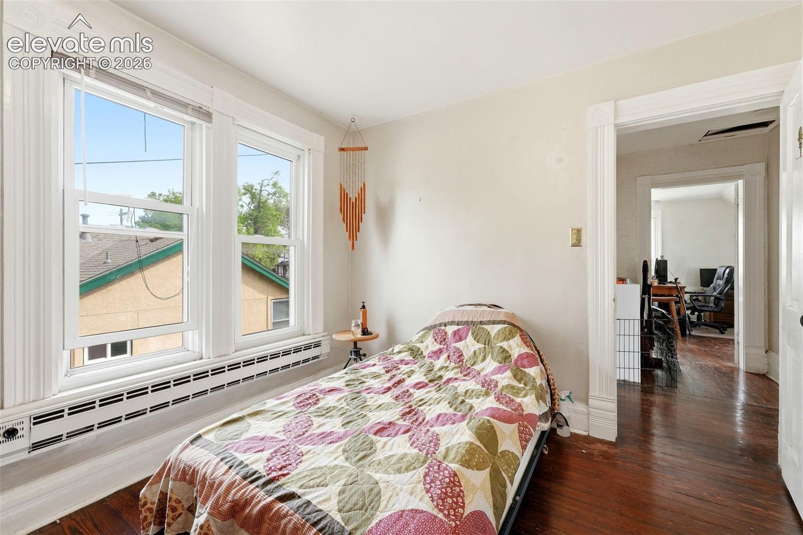Hardwood flooring throughout, two large windows with white trim, and a built-in baseboard heating unit