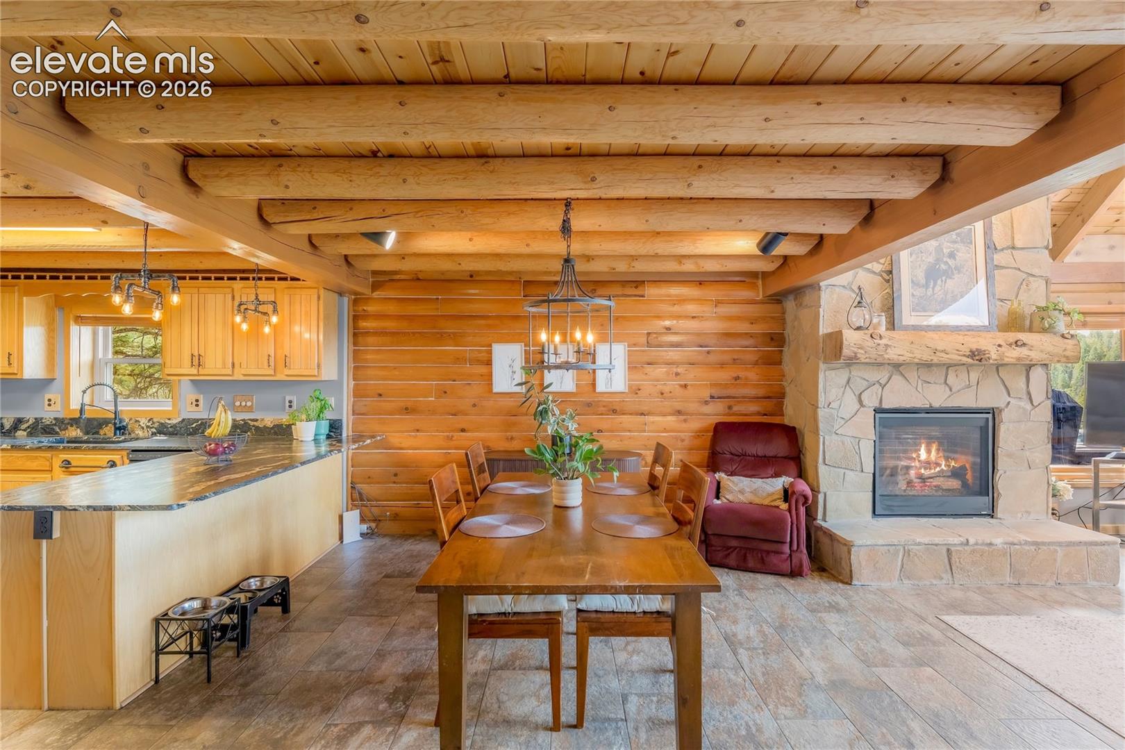 Exposed wood beam ceiling, wood-finish flooring, stone-clad fireplace with a wood mantel, wood paneling, and an island with a dark countertop