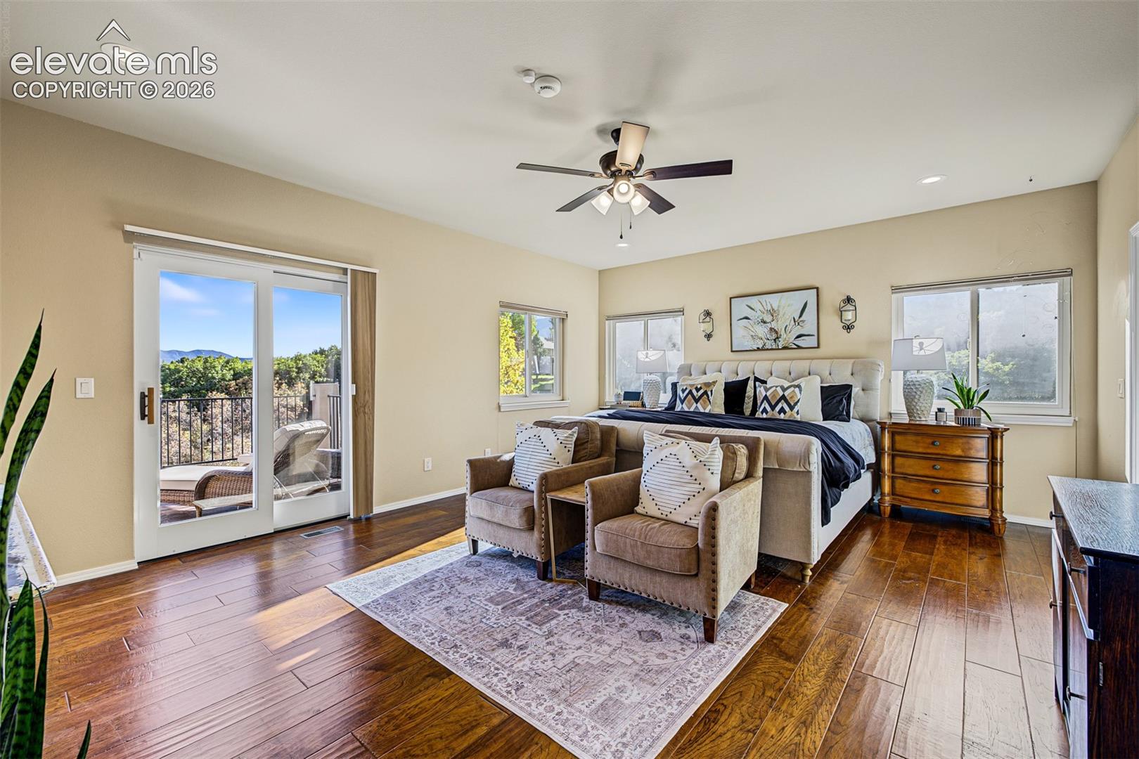 Spacious primary bedroom featuring hardwood flooring, abundant natural light, a ceiling fan, mountain views, and sliding glass doors opening to the rear deck.